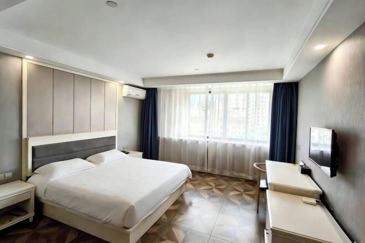 Ein modernes Hotelzimmer mit einem großen Bett, Nachttischen, einem Fernseher und einem Fenster mit Vorhängen.