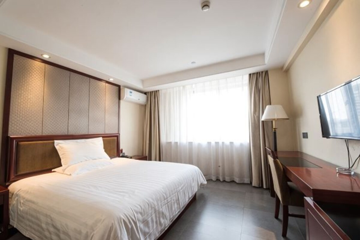 A hotel room with a large bed, a desk, a chair, a TV, and a window with curtains.