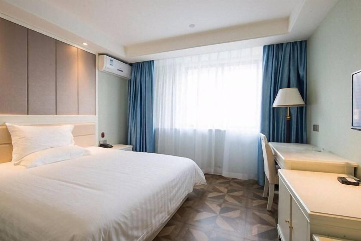 Ein Hotelzimmer mit Bett, Schreibtisch, Stuhl, Lampe und Klimaanlage.