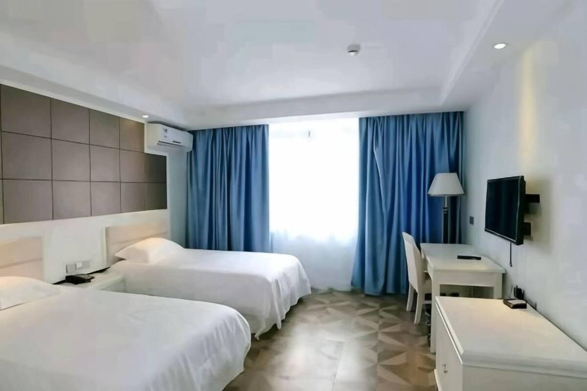 Ein Hotelzimmer mit zwei Betten, einem Schreibtisch, einem Sessel, einem Fernseher und einem Fenster mit Vorhängen.