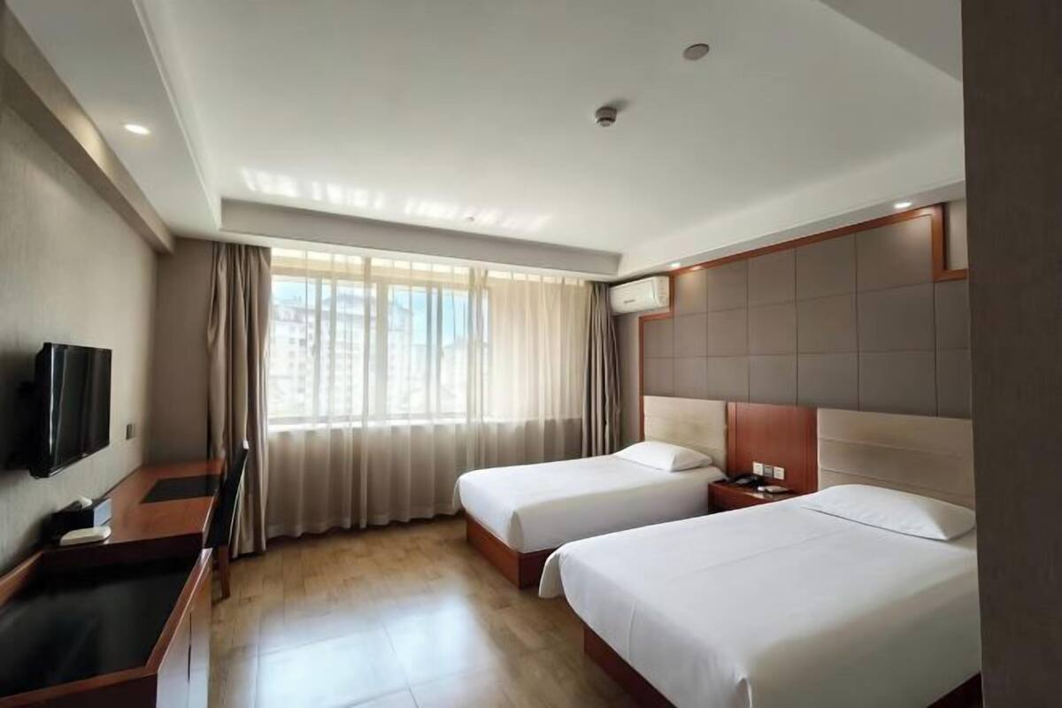 Ein Hotelzimmer mit zwei Betten, einem Schreibtisch, einem Flachbildfernseher und einem Fenster mit Vorhängen.