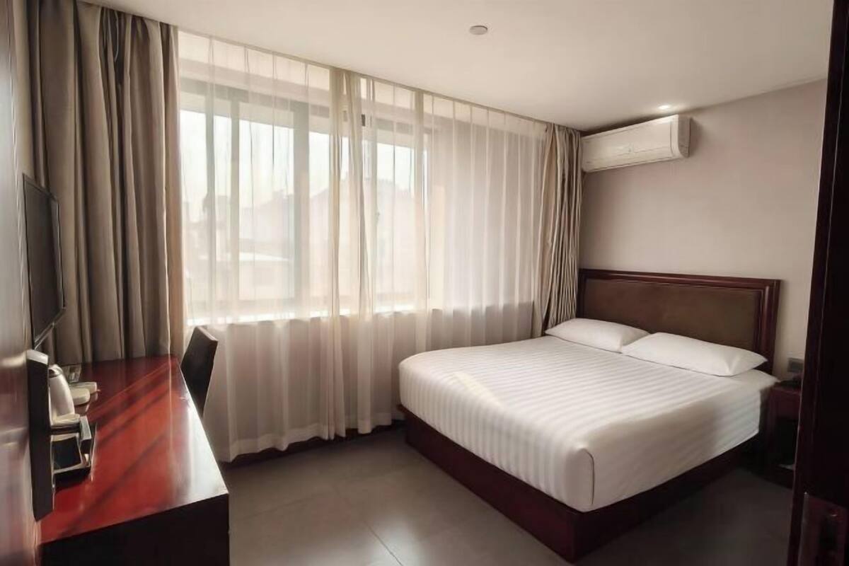 Ein Hotelzimmer mit einem großen Bett, einem Schreibtisch mit Stühlen, einem Fernseher und einem Fenster mit Vorhängen.