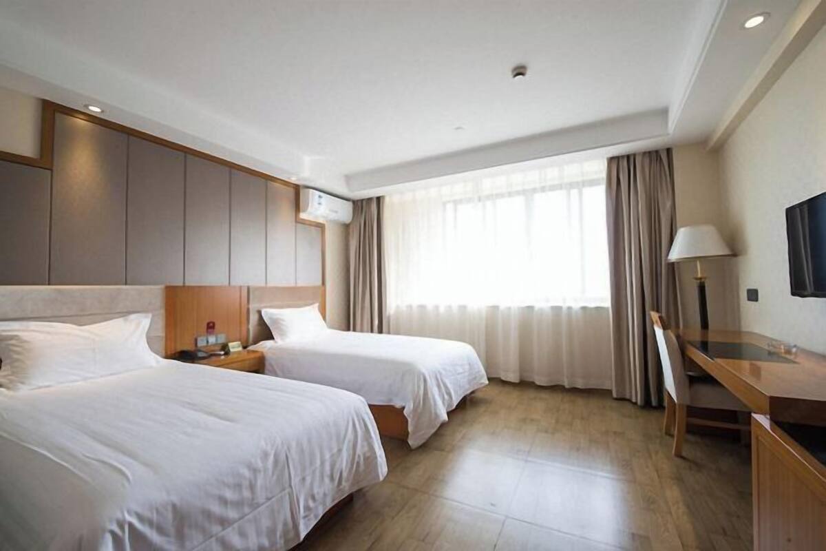 Ein Hotelzimmer mit zwei Betten, einem Schreibtisch, einem Sessel, einem Fernseher und einem Fenster mit Vorhängen.