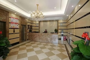 En hotellobby med et ternet gulv, en receptionsdisk, en lysekrone og en receptionist.