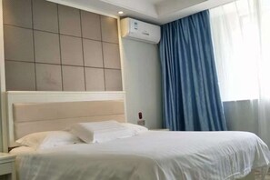 Une chambre d’hôtel avec un lit, une table de chevet, un climatiseur fixé au mur et une fenêtre avec des rideaux.