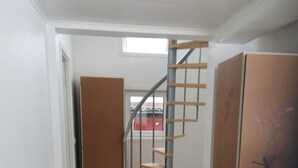 Un pasillo con piso de madera, un tapete estampado, una escalera con barandilla de metal y una puerta.