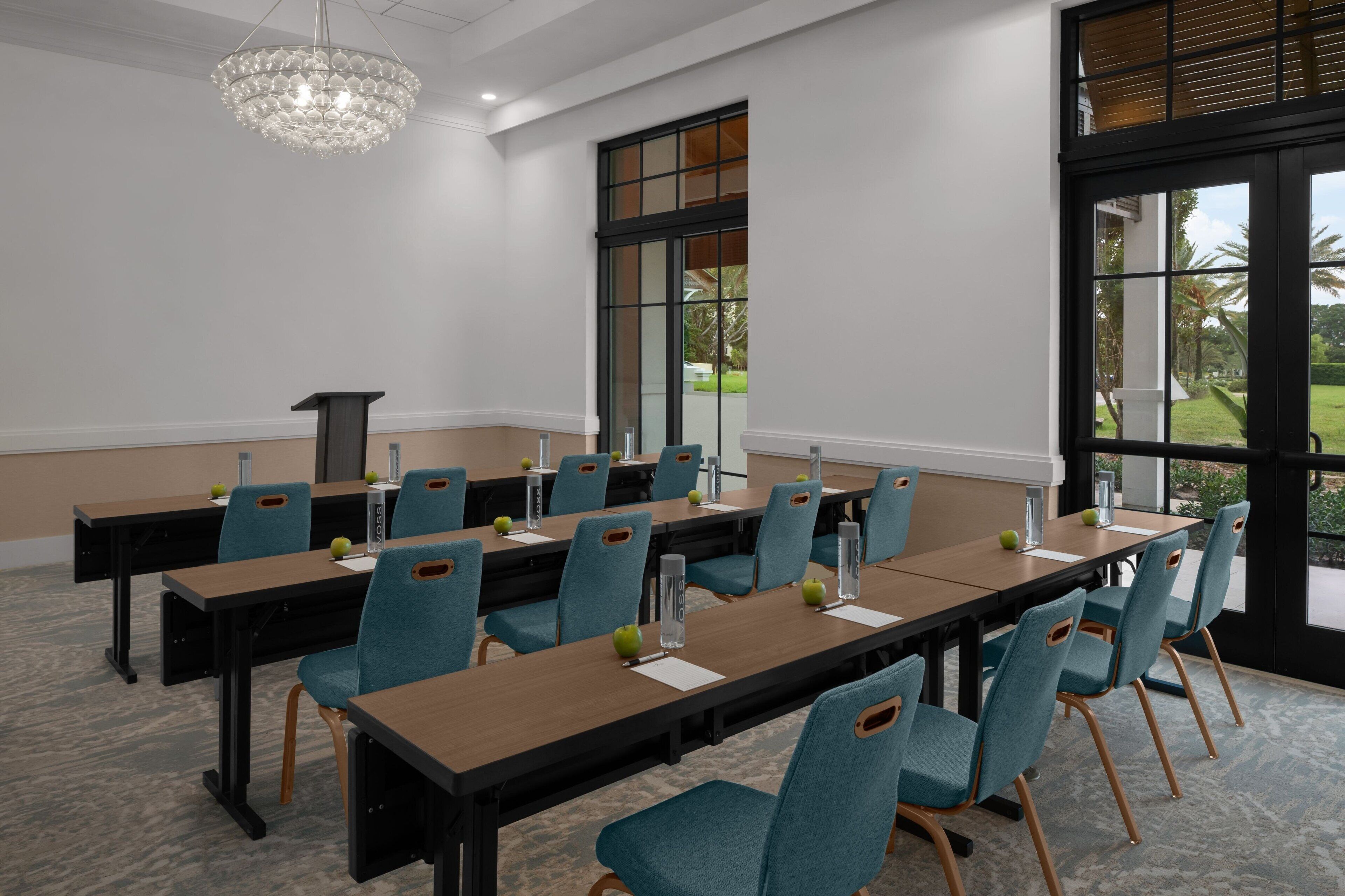 A conference room with a long table, chairs, a podium, and a chandelier.