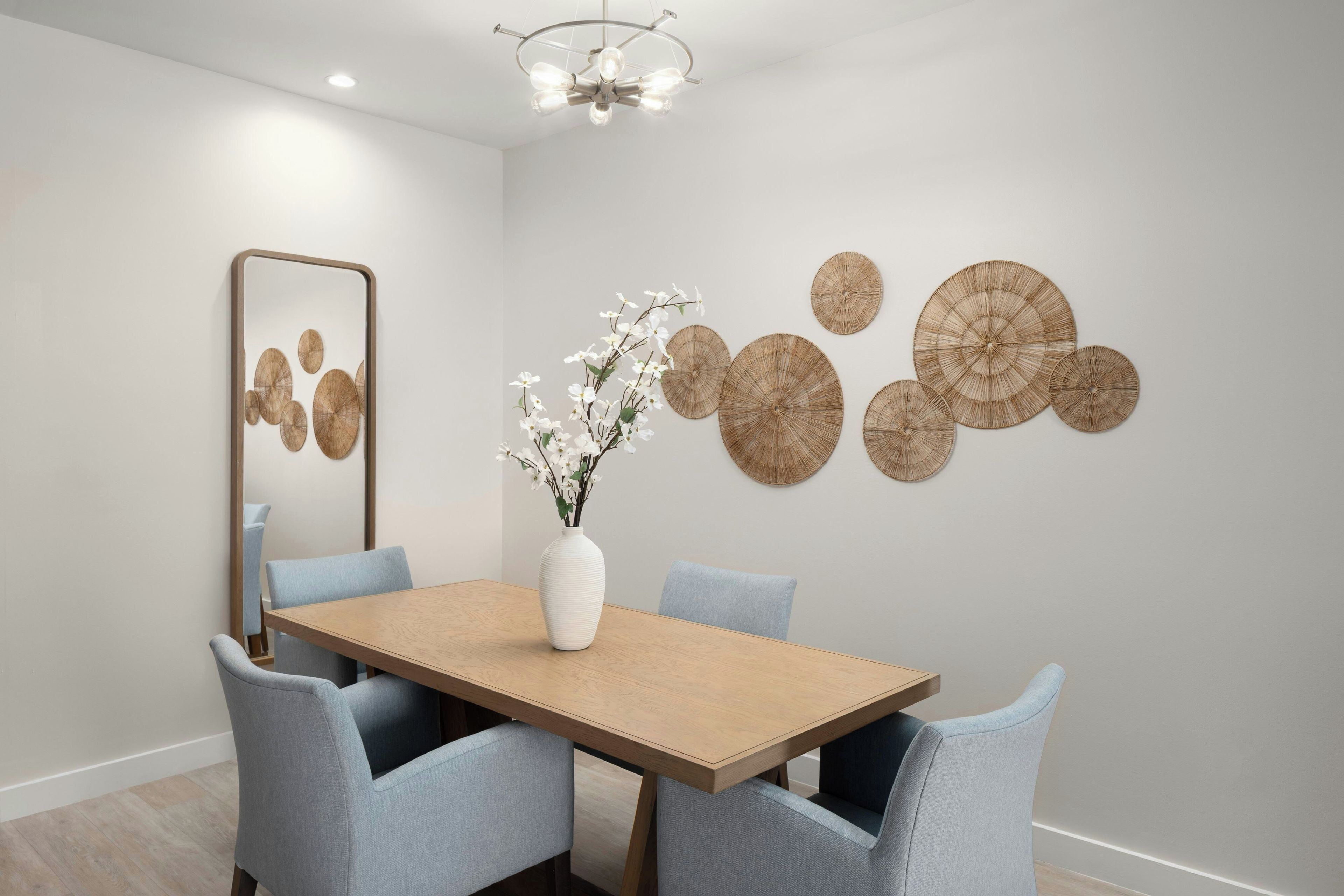 A dining room with a wooden table, six chairs, a vase with flowers, a mirror, and wall art.