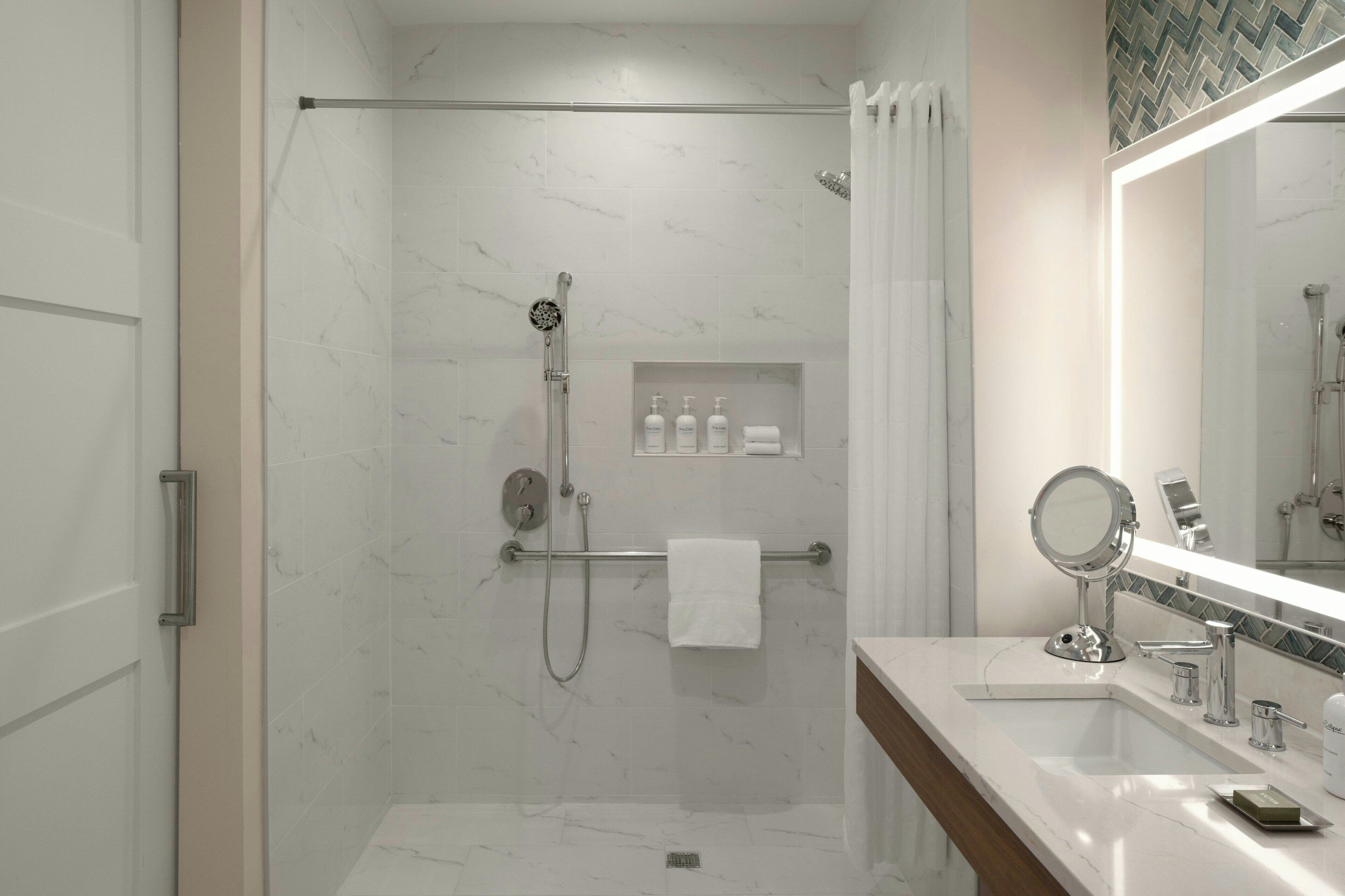 A modern bathroom with a glass-enclosed shower, a vanity with a mirror, and a shelf with toiletries.