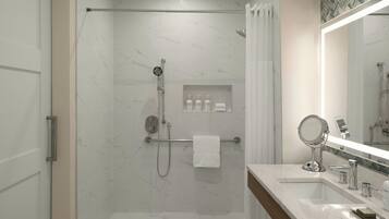 A modern bathroom with a glass-enclosed shower, a vanity with a mirror, and a shelf with toiletries.