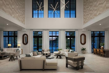 A dining area with a large table set for six, a flat-screen TV mounted on the wall, and a view of the outdoors through large windows. at The Belgrove Resort & Spa, West Palm Beach, Autograph Collection