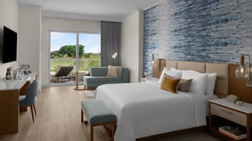 A hotel room with a large bed, a desk with a chair, a small table with a chair, and a view of the outdoors.
