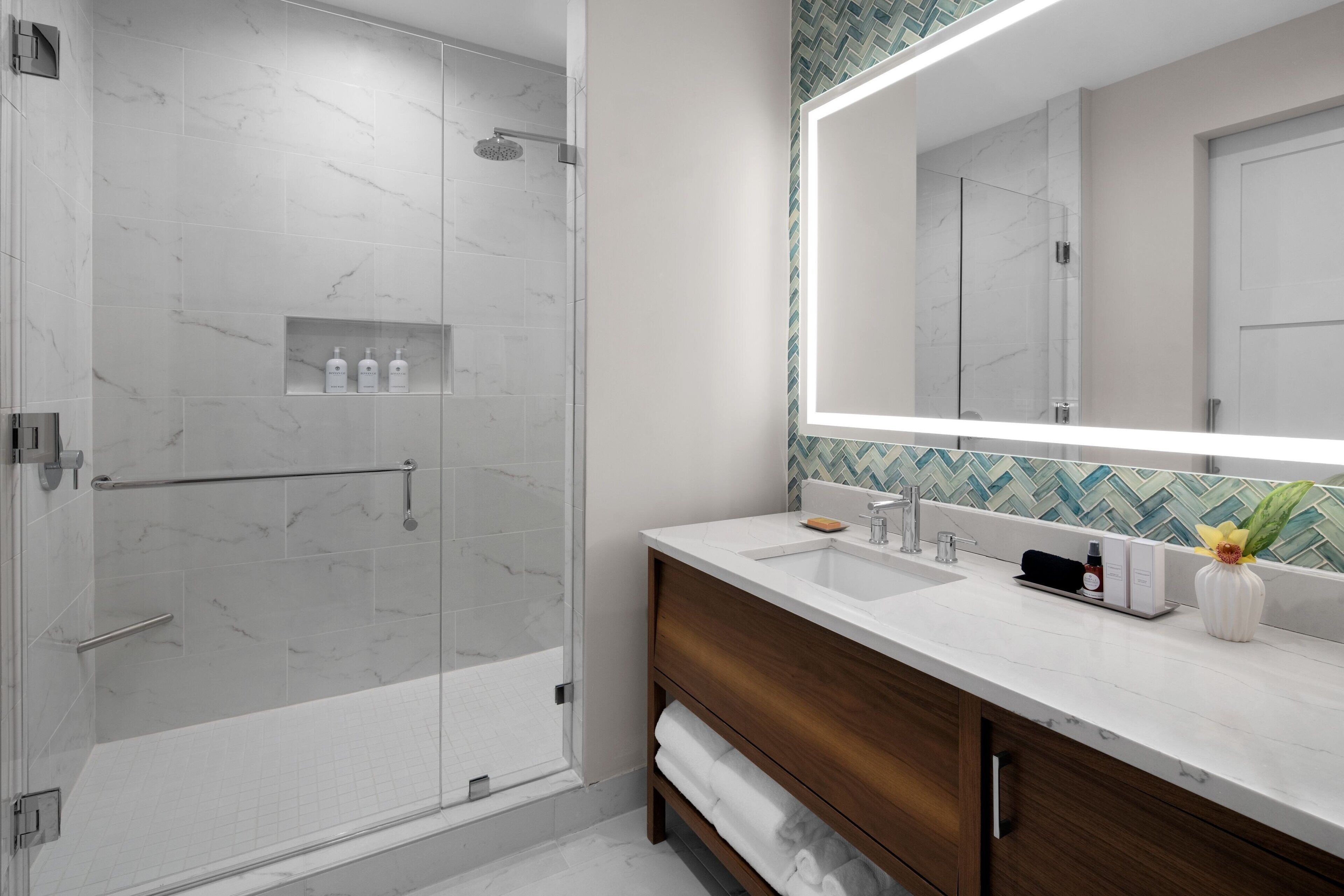 Une salle de bain moderne dotée d’une douche à parois de verre, d’un grand miroir et d’un meuble-lavabo avec un plan de travail en marbre.