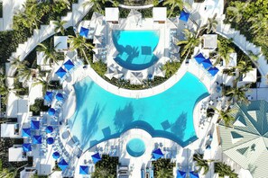 Luchtbeeld van een resort met een centraal zwembad, omringd door liggedeeltes met parasols en ligbedden.