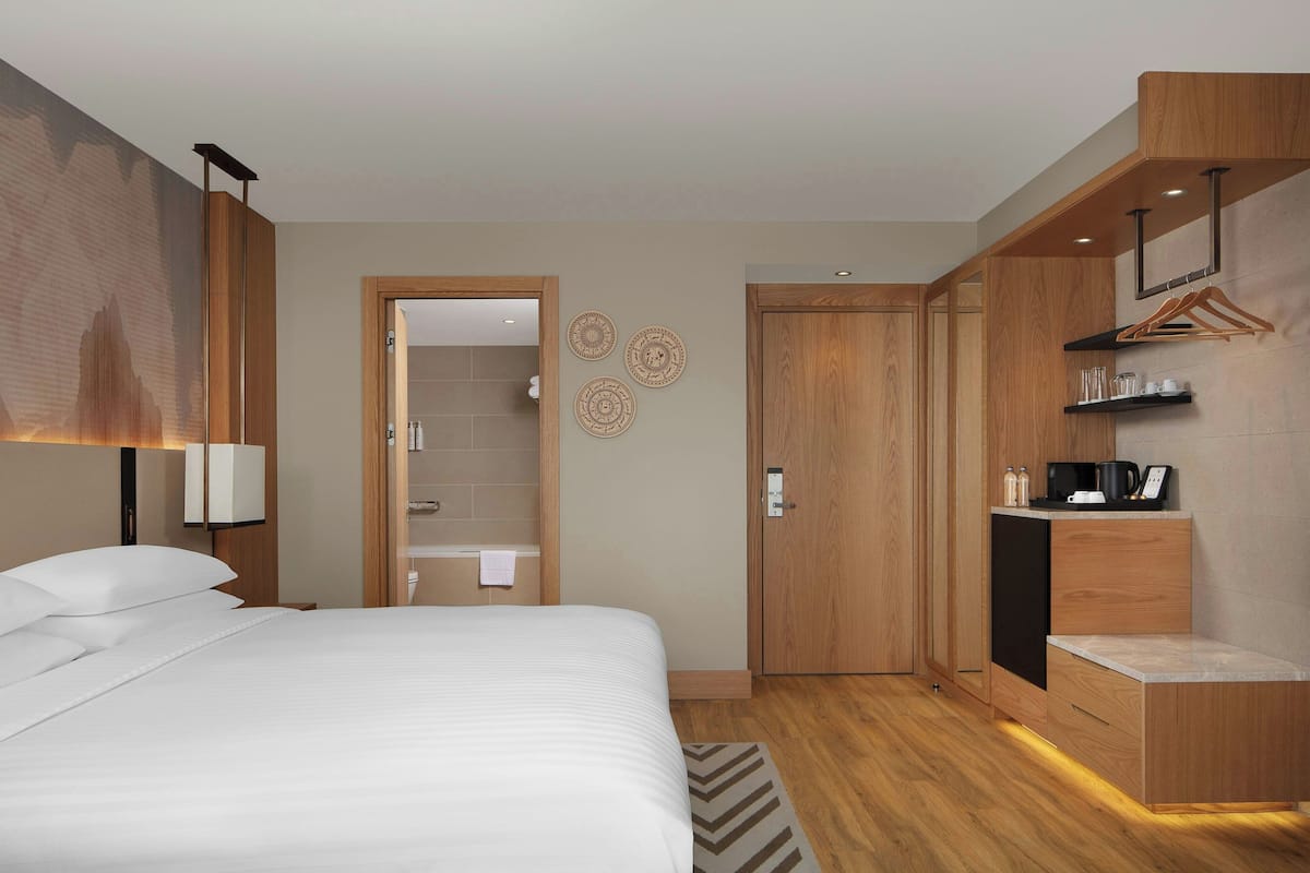 A modern hotel room with a large bed, wooden wardrobe, and a built-in desk with a coffee machine.