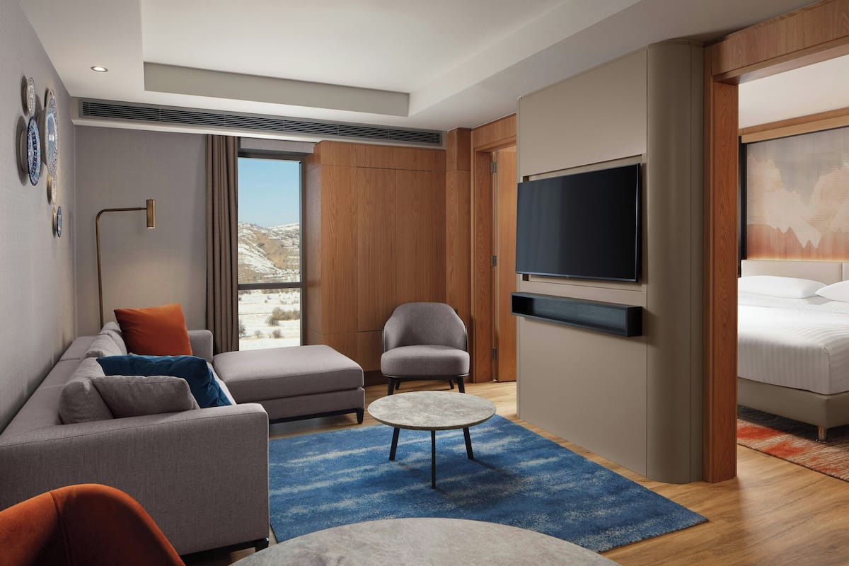 A modern hotel room with a sofa, armchair, round coffee table, and a bed.