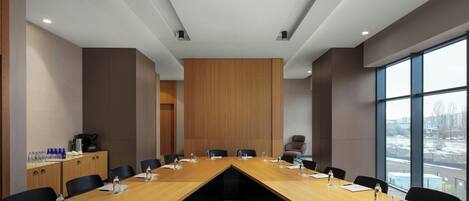 A conference room with a long table, chairs, and a view through large windows.