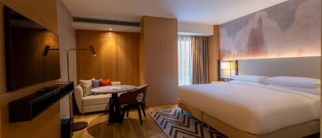 A hotel room with a bed, a desk with a chair, a TV, and a large painting on the wall.