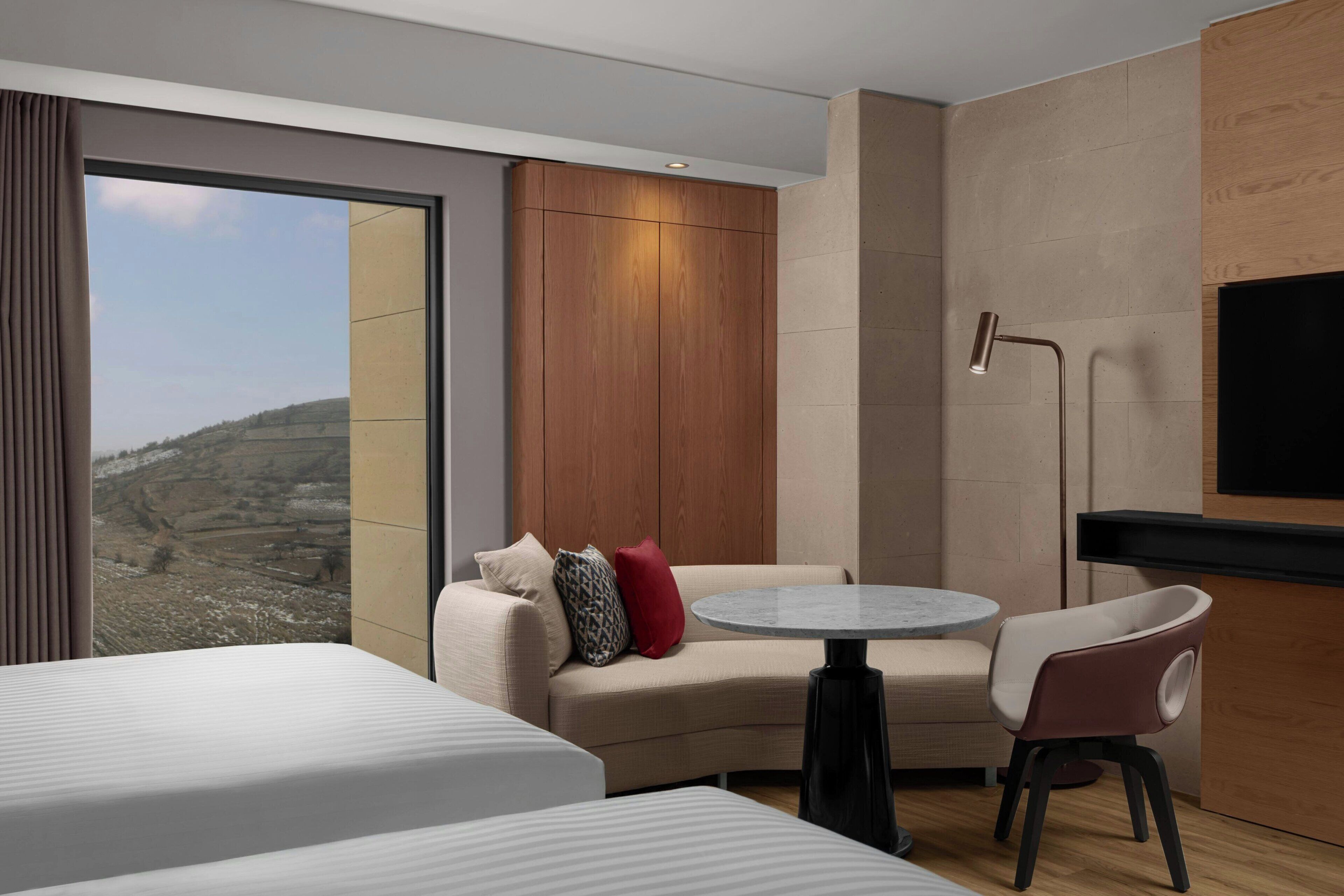 A modern hotel room with a large window, a sofa, a round table, and a TV.