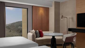 Una habitación de hotel moderna con un ventanal grande, un sofá, una mesa redonda y un televisor.
