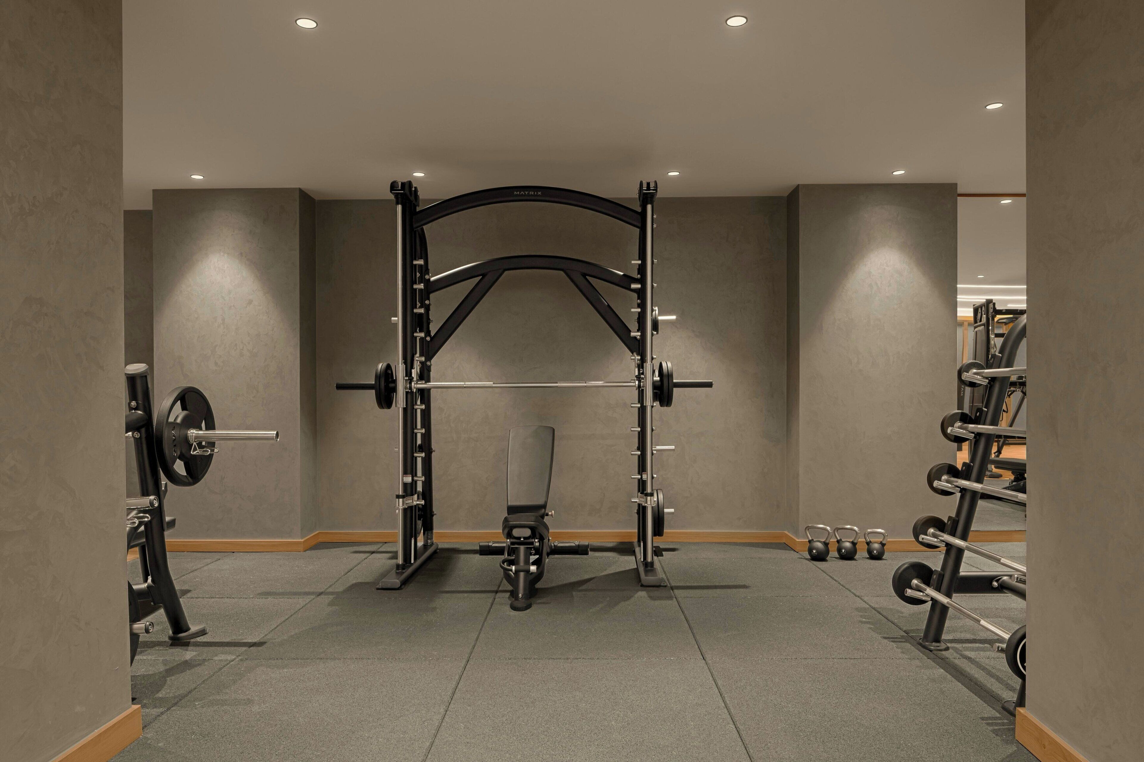 Un gimnasio con una estructura para sentadillas, banca de pesas y discos de peso.