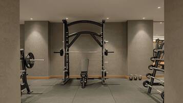 Un gimnasio con una estructura para sentadillas, banca de pesas y discos de peso.