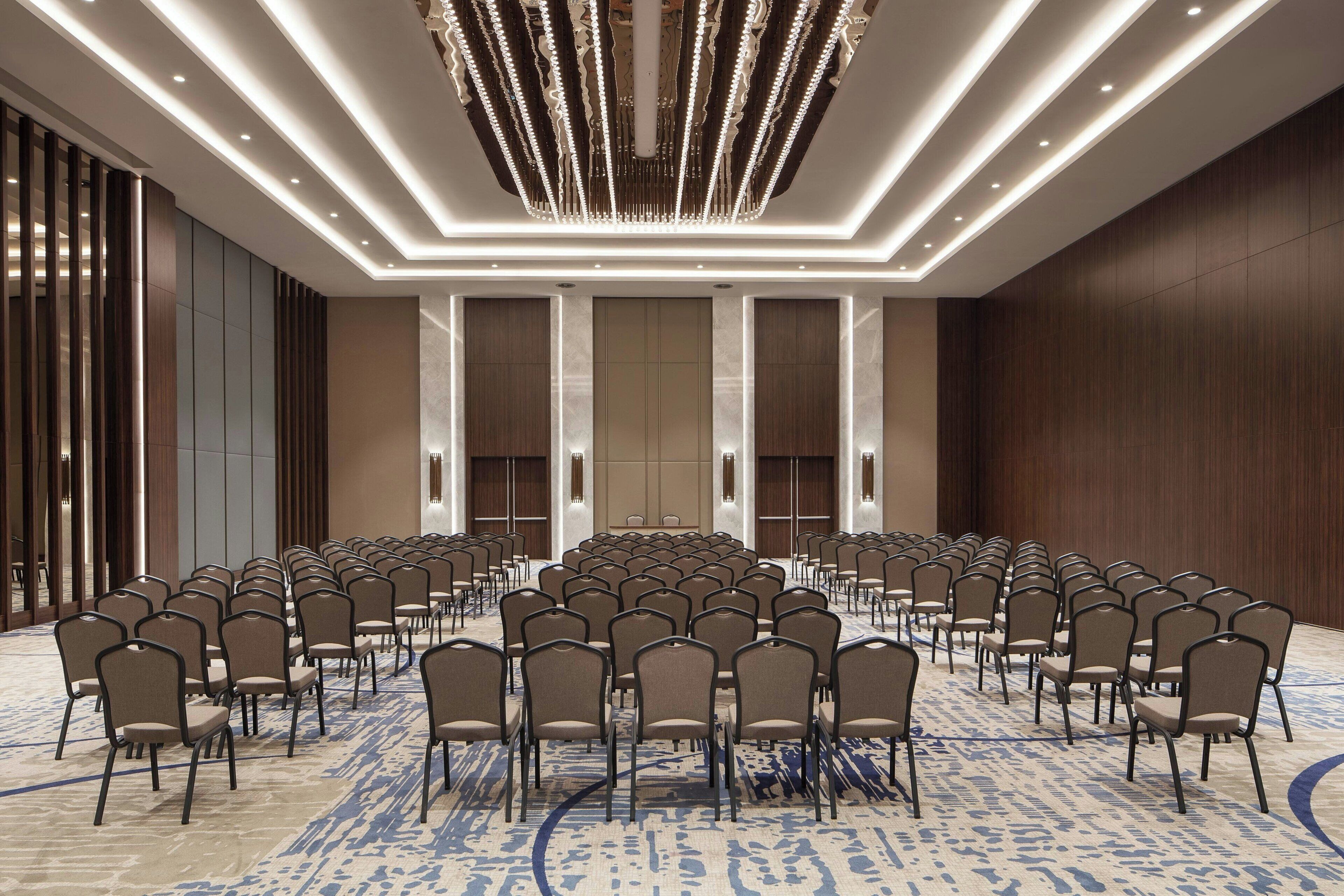A conference room with rows of chairs, a patterned carpet, and a modern chandelier.