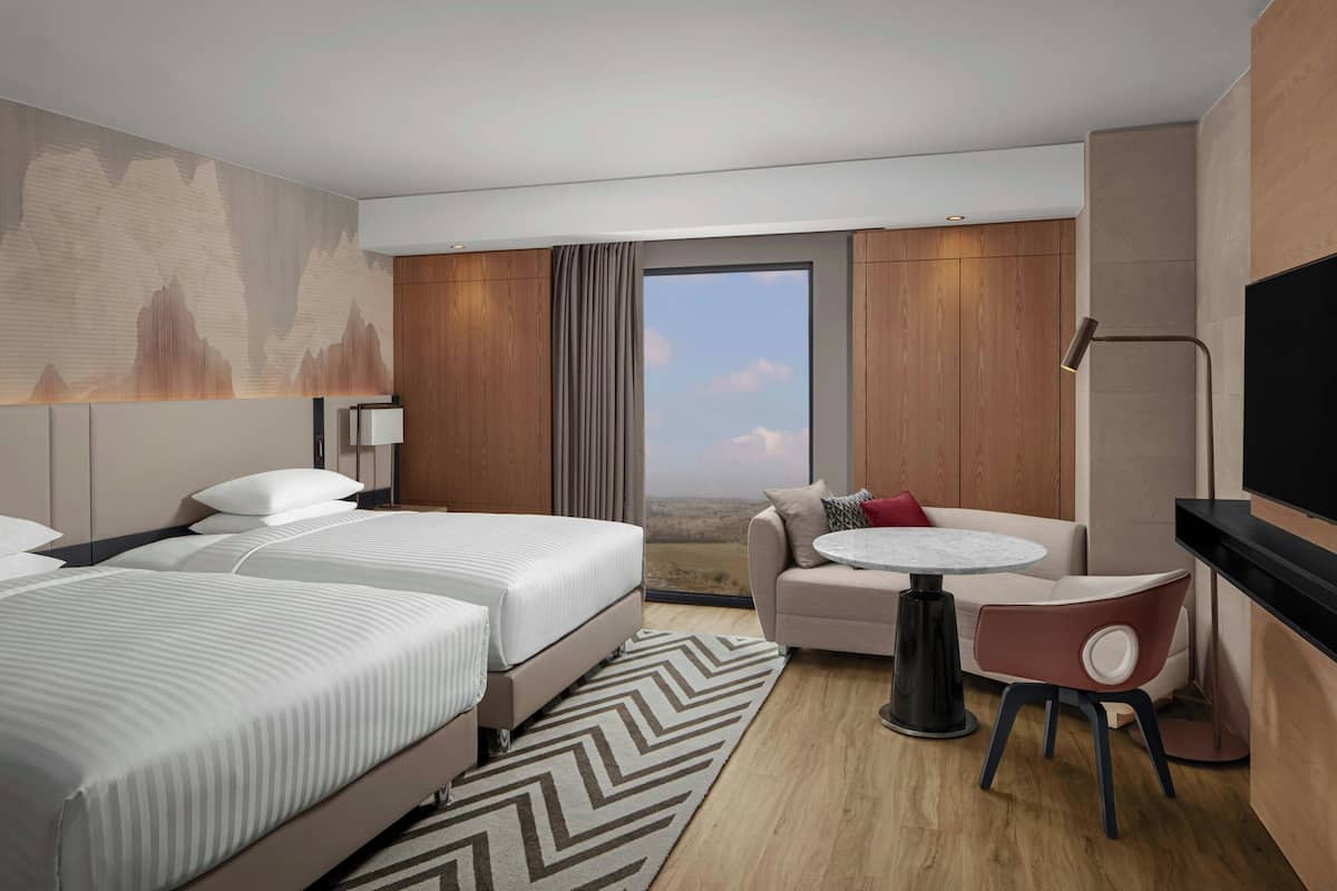A modern hotel room with two beds, a sofa, a small round table, and a TV.