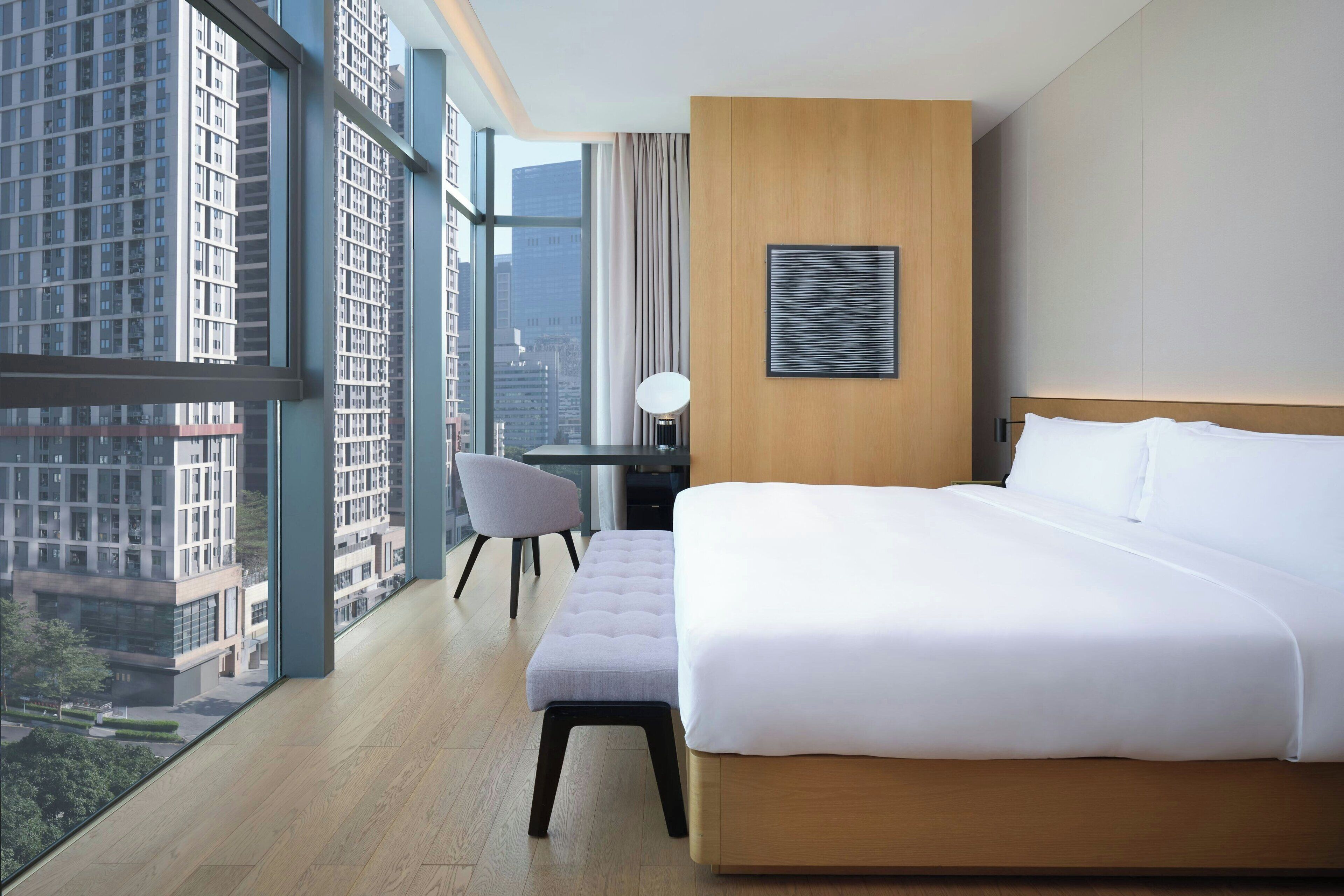 A hotel room with a large window, a bed, a desk, and a chair.