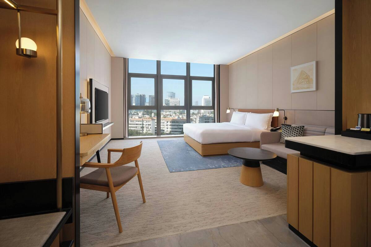 A hotel room with a large bed, a desk with a chair, a small table, and a TV.