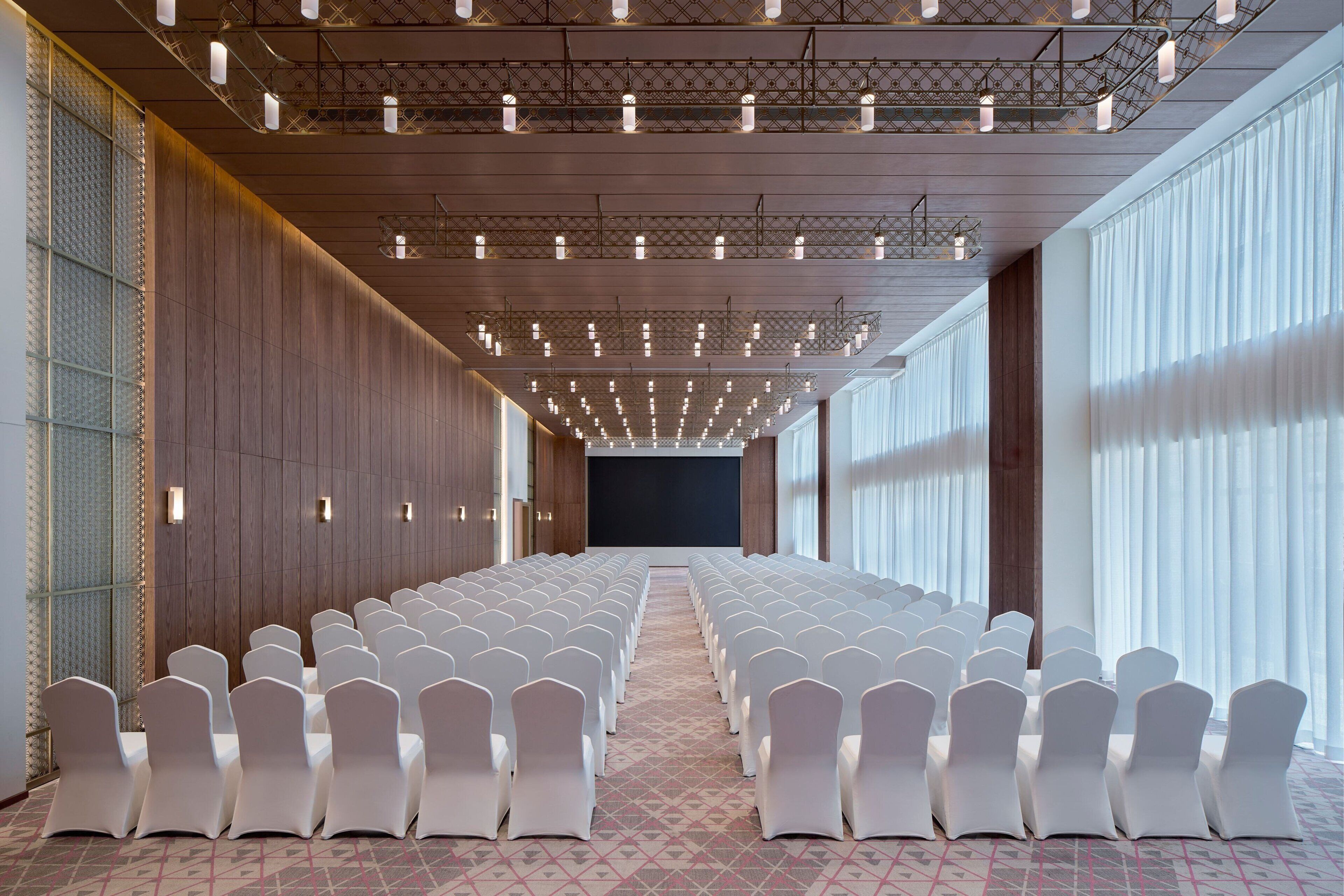 Une salle de conférence avec des rangées de chaises blanches, une moquette à motifs et un grand écran à l’avant.