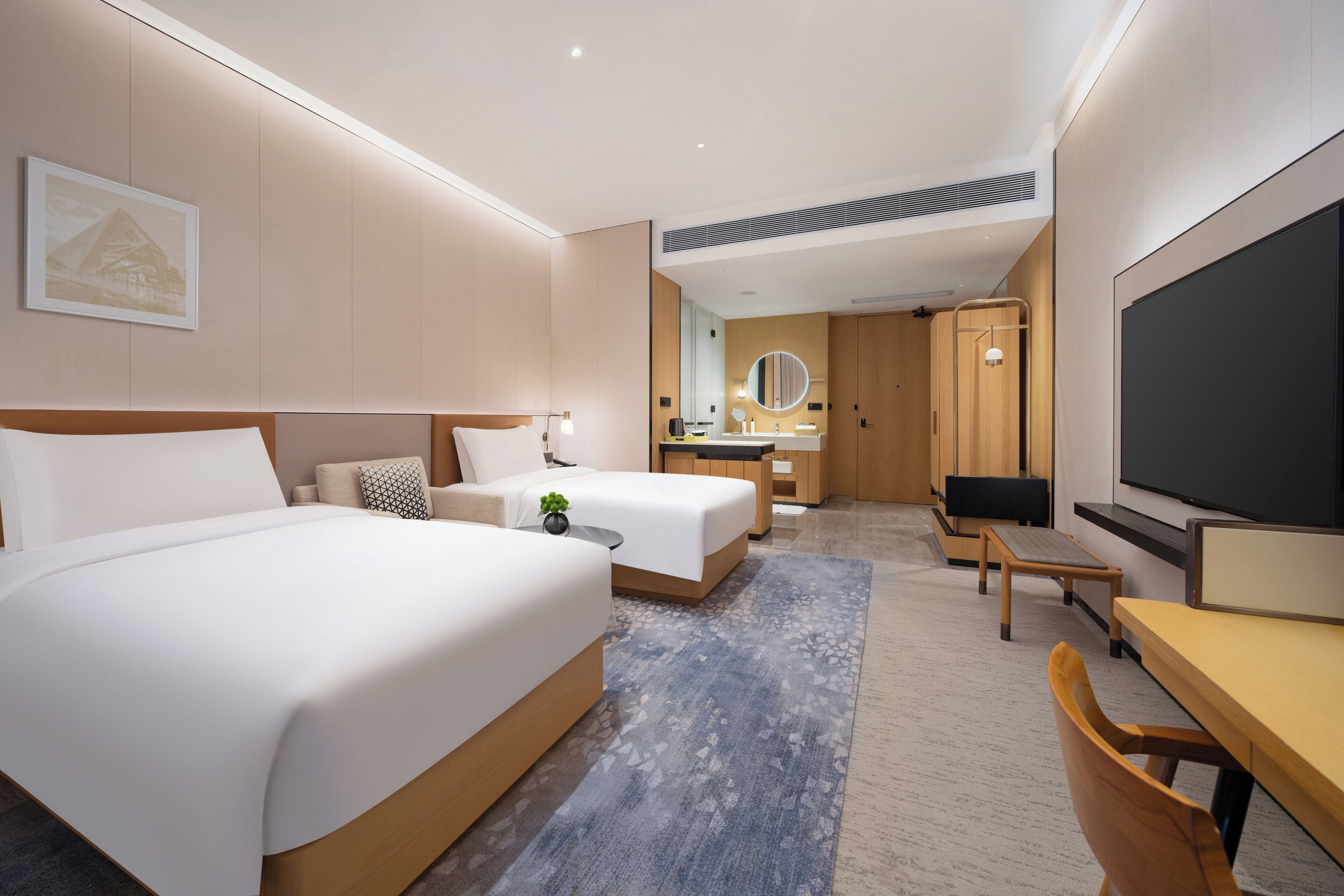Una camera d'hotel moderna con due letti, una scrivania, una TV e un bagno con specchio e lavandino.