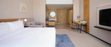 Una habitación de hotel moderna con una cama grande, un escritorio, un televisor y un baño visible a través de una puerta abierta.