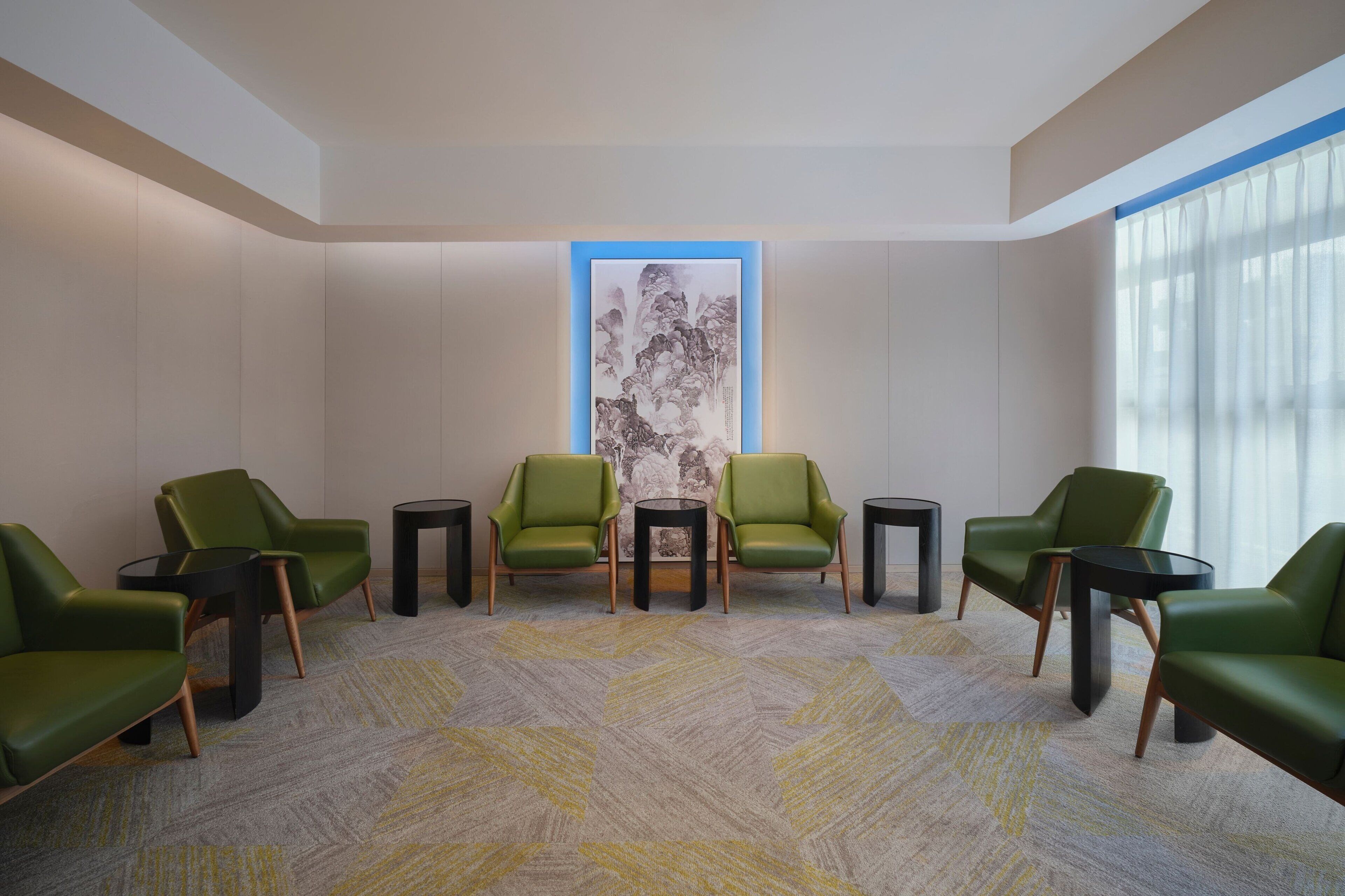 Een moderne wachtruimte met groene stoelen en zwarte tafels, een groot abstract schilderij aan de muur en een kamerbreed tapijt met een patroon.