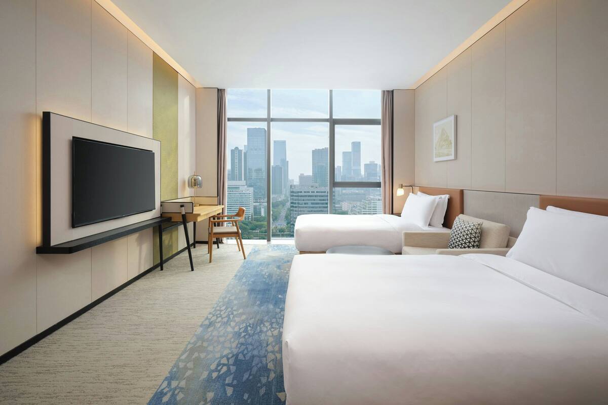 A hotel room with a large TV, two beds, a desk, and a view of the city skyline.