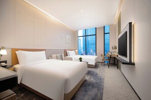 Habitación de hotel con una cama grande, un escritorio con una silla, un televisor y una ventana con vistas a la ciudad.