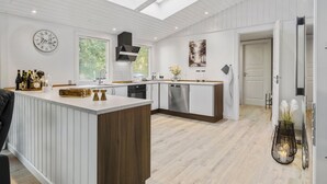 Une cuisine moderne dotée d’un îlot central, de fenêtres de toit, d’une horloge et offrant une vue sur la verdure environnante.
