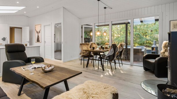 Un salon moderne avec une table basse en bois, un pouf recouvert de fourrure et un coin repas comprenant une table et des chaises en bois.