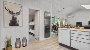 Une cuisine moderne avec des meubles blancs, un îlot central et un coin repas agrémenté d’une chaise recouverte de fourrure.