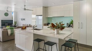 A modern kitchen with white cabinets, a central island with stools, and a dining area with a sofa and a TV.