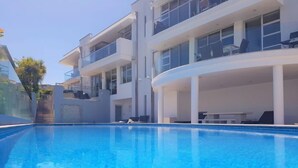 A modern hotel with a swimming pool, multiple balconies, and a covered outdoor seating area.