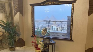 Ein Zimmer mit einem großen Fenster, einem dekorativen Tisch mit Vase und Blumen, einer Chandelüster und Blick auf Pyramiden.