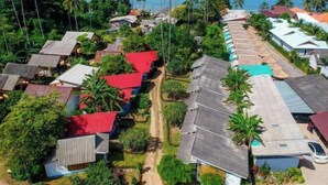 An aerial view of a coastal village with houses, some with red roofs, and palm trees. - Isara Lanta Beach Resort (Koh Lanta)
