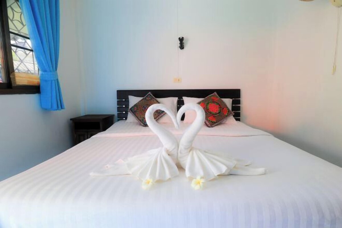 A bed with two swan-shaped pillows and a window with blue curtains.