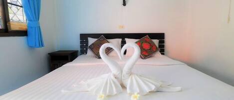A bed with two swan-shaped pillows and a window with blue curtains.