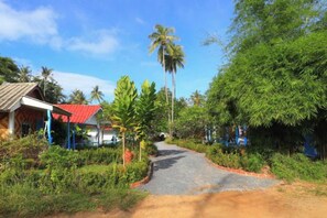 A rural road leading to a house with a red roof, surrounded by greenery and palm trees. - Isara Lanta Beach Resort (Koh Lanta)