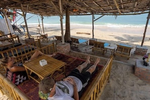 A beachside lounge with wicker furniture, a wooden table, and a view of the ocean. - Isara Lanta Beach Resort (Koh Lanta)