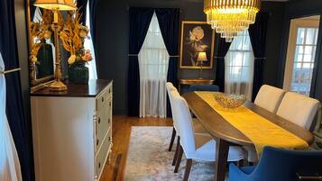 A dining area with a wooden table, white chairs, a chandelier, and a mirror with flowers.