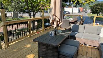 A wooden deck with outdoor furniture, including a table and a sofa, surrounded by a wooden railing.