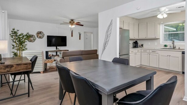 Een moderne keuken met witte kasten, een eetgedeelte met een grote tafel en stoelen, en een zithoek met een bank en televisie.